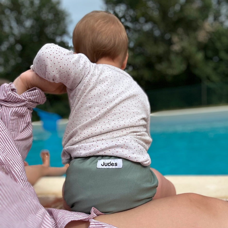 Bebé Judes en el regazo junto a la piscina con pañales o pants